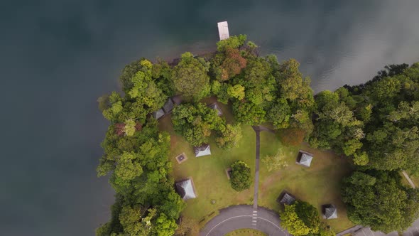 Moving drone video looking down on a lush park area next to a volcanic crater lake with clouds refle alt