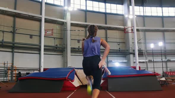 Pole Vaulting in the Indoors Stadium - Young Woman with Pigtails Jumping Over the Bar and Falling alt
