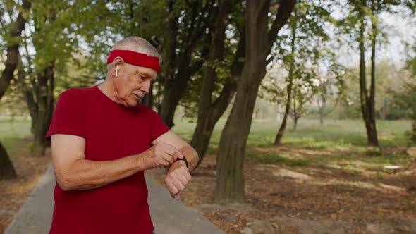 Senior Sport Man Starting Smart Watch Timer, Tracking Distance and Start Running in Public Park alt