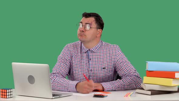 A Man Sits at a Desk in Front of a Laptop Takes Notes Then Puts a Pen to His Upper Lip Making a alt