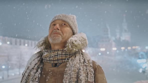 An Elderly Man Enjoys Snowfall in the City on Christmas Eve or New Year's Eve