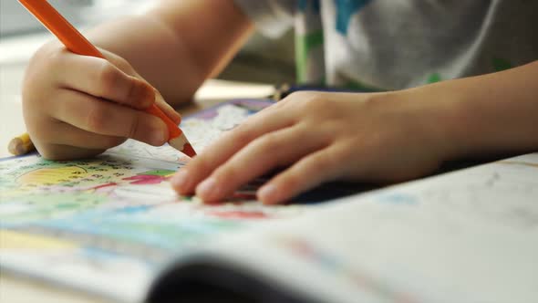 Child hands paints a orange pencils on a paper