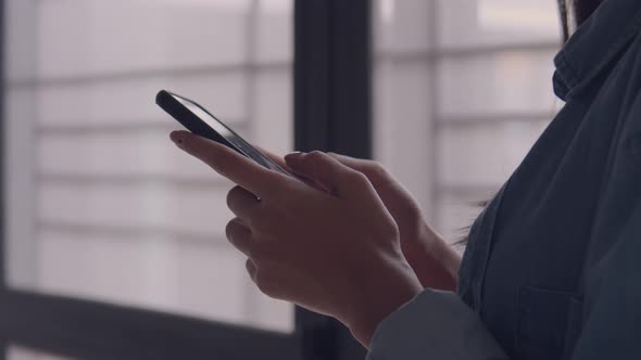 Asian businesswoman holding typing mobile phone and scrolls through social media feed in smartphone.