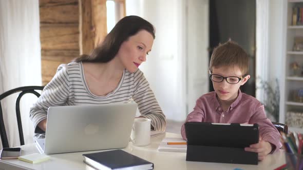 European Woman is Helping Son Who Learning Online with Tablet at Table in Apartment Room Spbd alt