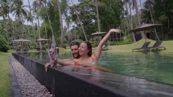 A Static Shot of a Happy Young Couple Taking Selfie Photo at Edge of Swimming Pool alt