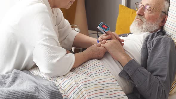 Senior Woman Apply at Sick Husband's Fingertip Pulse Oximeter Check Pulse Rate