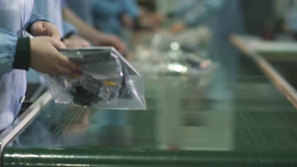 Workers pack a kit for a home TV on a factory assembly line alt