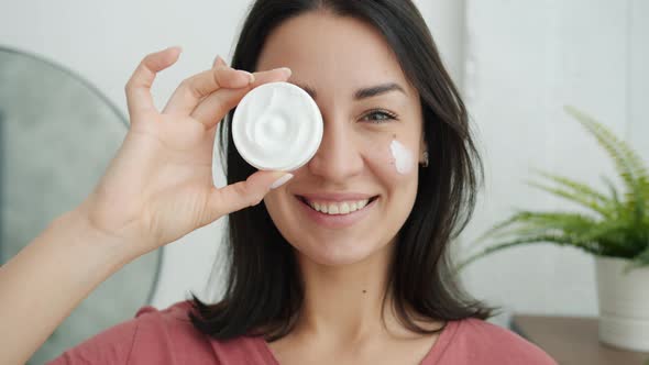 Portrait of Beautiful Girl Holding Face Cream Smiling and Looking at Camera in Bathroom alt