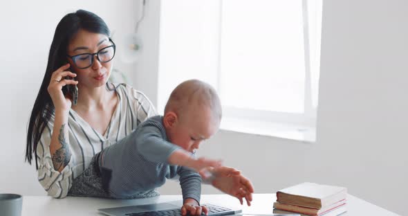 Young Mother Freelancer with Her Child Working at Home Office Using Laptop alt