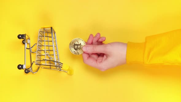 Vertical video Female hand putting golden shiny bitcoin into mini grocery cart