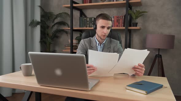 Young Smiling Man Employee Doing Paperwork in the Office at the Computer. Male Worker Looking with alt