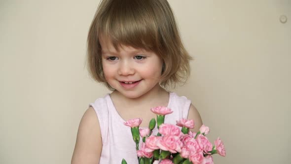 Little Girl Holds Bouquet of Flowers Pink Carnations Looks at Camera Smiles and Smells Flowers alt