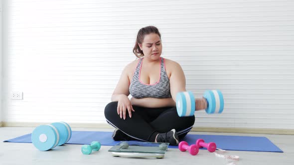 Young Asian woman overweight in sportswear exercise by lifting dumbbells while worry her weight