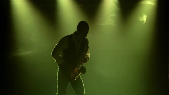 Silhouette a Young Stylish Guy Plays the Golden Shiny Saxophone in the Multicolored Spotlights on alt