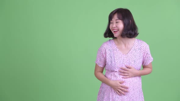 Happy Asian Pregnant Woman Showing Something and Looking Surprised alt