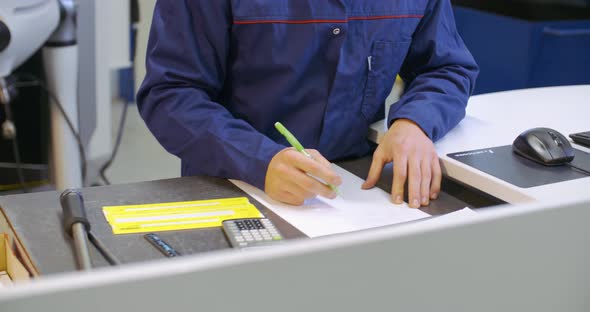 apprentice worker making calculations in factory at cnc machine alt