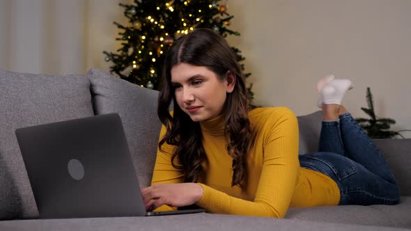 Woman Uses Laptop Online Chatting with Friends on Background Christmas Tree alt