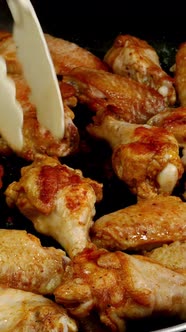 Many sprinkled with spices sliced chicken wings, preparation and turning in hot frying pan.