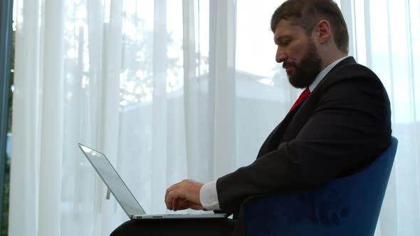 Serious Bearded Businessman Working on Laptop Computer in Office Lobby alt