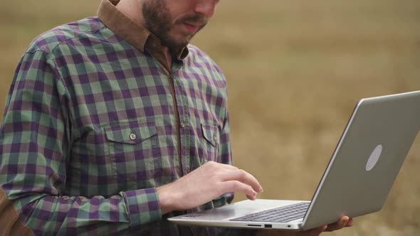 Handheld Farmer Man Stands in the Field of Rye and Works on a Laptop Investigating Plants Ecologist alt