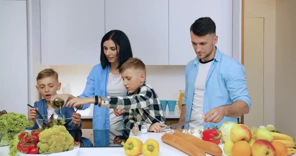 Family of Parents and Their Sons Cooking Together Fresh Vegetable Salad at the Table alt