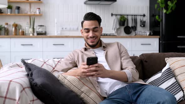 Positive Handsome Indian or Arabian Guy in Trendy Clothes Sitting in a Modern Living Room on alt