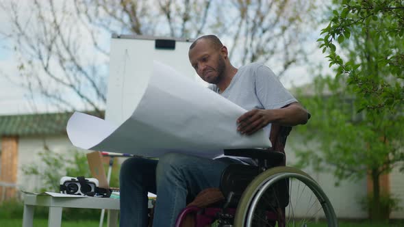 Serious Smart Skilled Architect in Wheelchair Looking at Blueprint Shaking Head alt