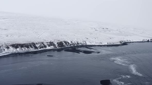 Drone Over Low Tide On Black Sand Beach Towards Snowy Landscape alt