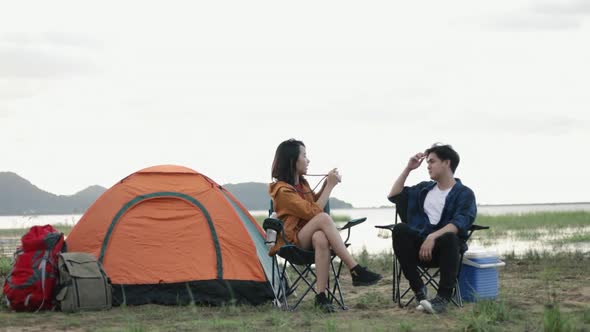 Young Asian couple camping use film camera taking a photo together on a vacation weekend.