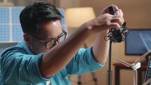 Close Up Of Asian Man Testing The Wind  Turbine While Working With Laptop Next To The Solar Cell alt