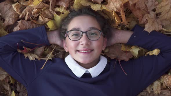 School Girl Lies on Autumn Leaves and Smiling at Park