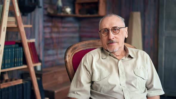 Portrait Smiling 70s Elderly Man in Eyeglasses Relaxing in Red Vintage Armchair Posing at Home alt