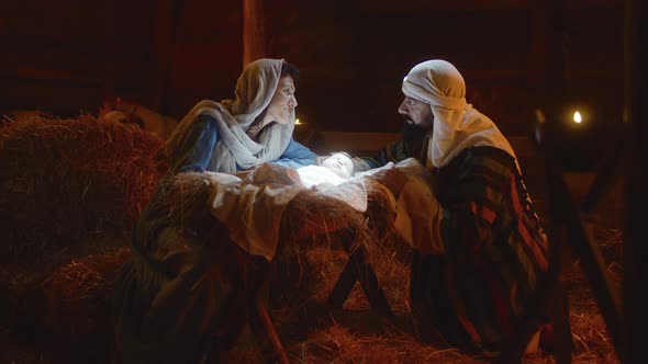 Mary and Joseph Caressing Baby Jesus in Illuminated Manger alt