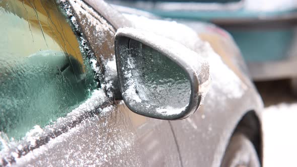 Close Up Of Right Side Mirror Of A Parked Car With Snow Defrosting alt