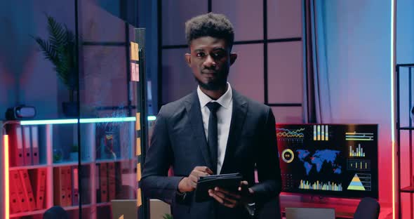 Businessman Working on Tablet PC in Evening Office and then Looking Into Camera with Sincerely Smile alt