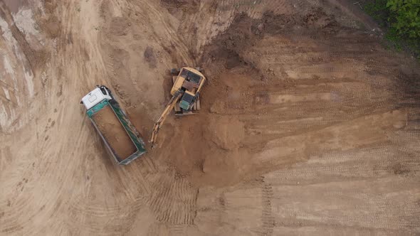 Aerial top view: yellow excavator pouring soil into tipper. alt