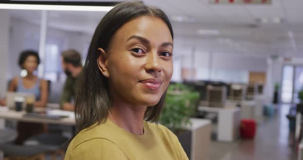 Portrait of happy biracial businesswoman over business colleagues in office alt
