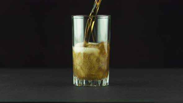 Cola Is Poured Into Glass Full of Bubbles and Foam Isolated on Black Background alt