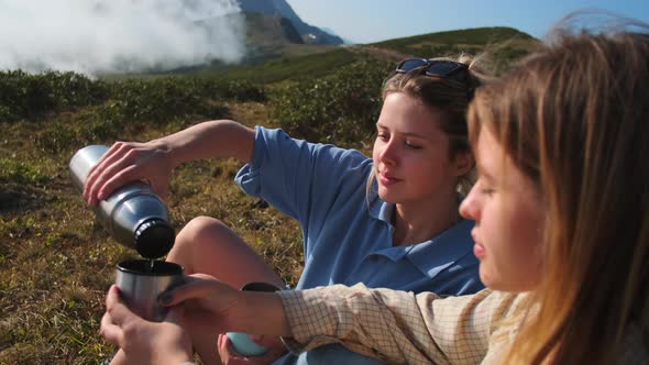 Halt at Top of Mountain Two High School Girls or Students are Resting and Drinking Tea From Thermos alt