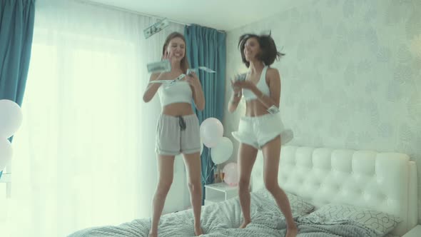 Two young beautiful smiling women in white pajamas making dollars rain alt