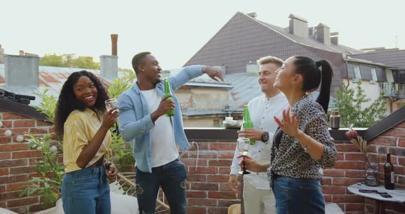 Stylish Joyful Multiethnic Youth Having Party on the Balcony with Beer Under Disco Dances alt