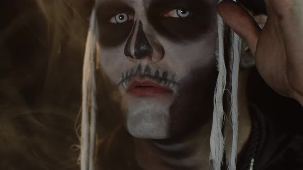 Close-up of Sinister Man with Skull Makeup Making Faces and Exhaling Cigarette Smoke From His Mouth alt