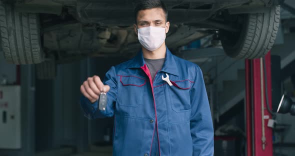 Customer Care Concept. Young Auto Mechanic in Protective Medical Mask Offering Keys To Camera alt