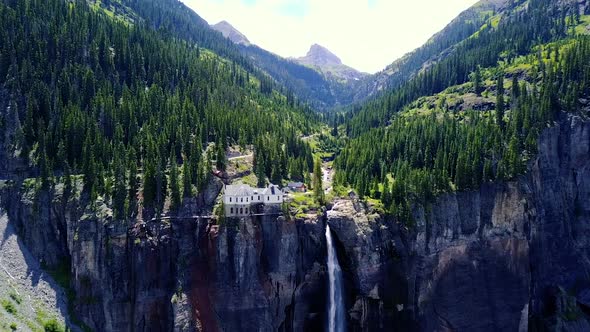 Aerial View of Drone Flying Toward Mountain Waterfall with Old Utility Lodge Next Door alt