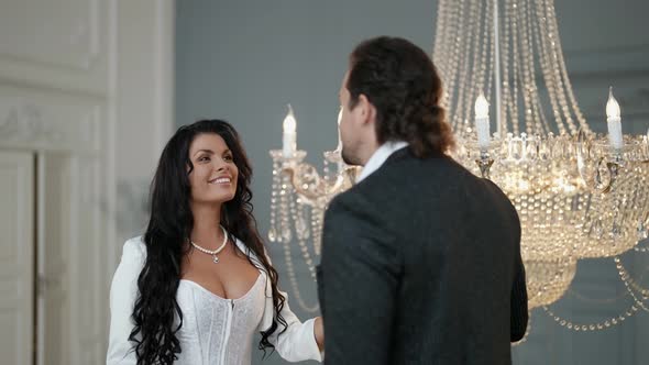 a Bride with Long Dark Hair and Big Breasts Touches the Pendants of a Crystal Chandelier and alt