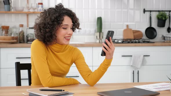 Smiling Curly Woman Student Greets Talking Listens Online Video Call Smartphone alt