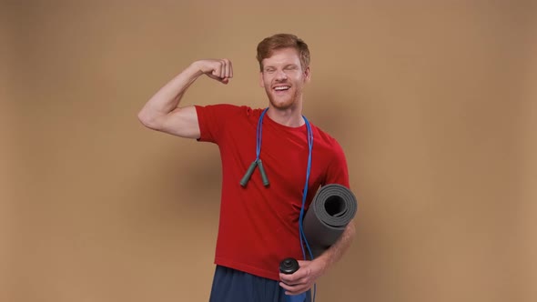 Funny Young Man in Sportswear Show Biceps Isolated on Beige Background alt