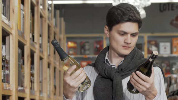 Attractive Young Man Choosing Between Two Bottles of Wine to Buy alt