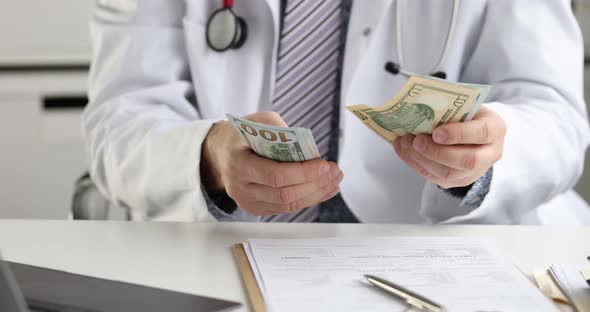 Male Doctor Sitting at Table and Counting Dollar Bill  Movie Slow Motion alt