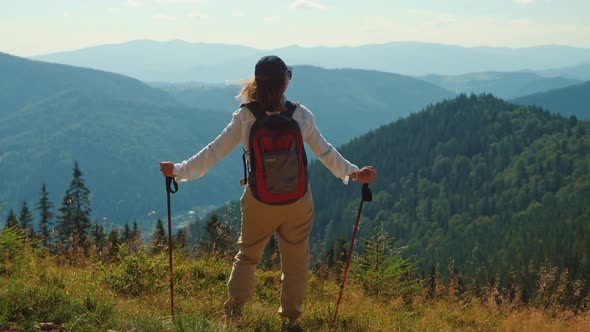 Girl with Trekking Poles Standing on the Top of the Mountain